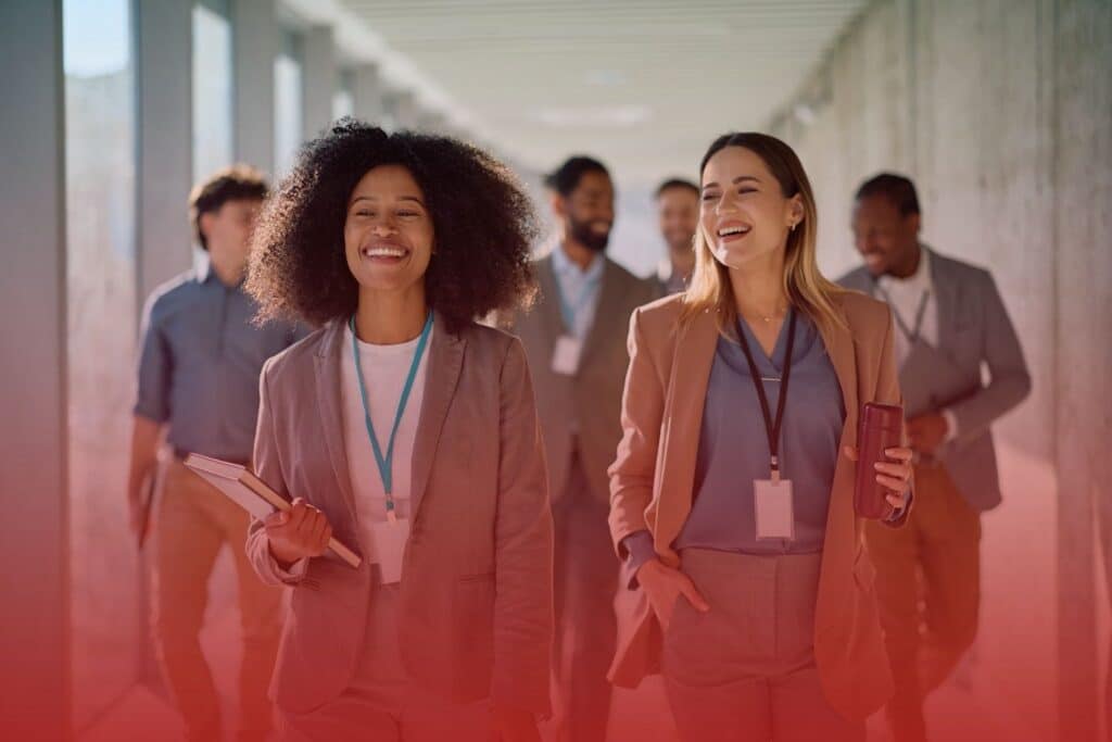 Group of smiling business professionals walking together down a modern office hallway.
