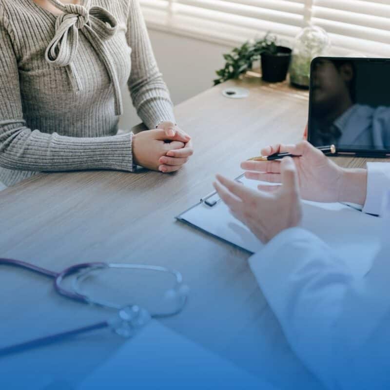 Patient sitting across a desk from a doctor during a medical consultation.