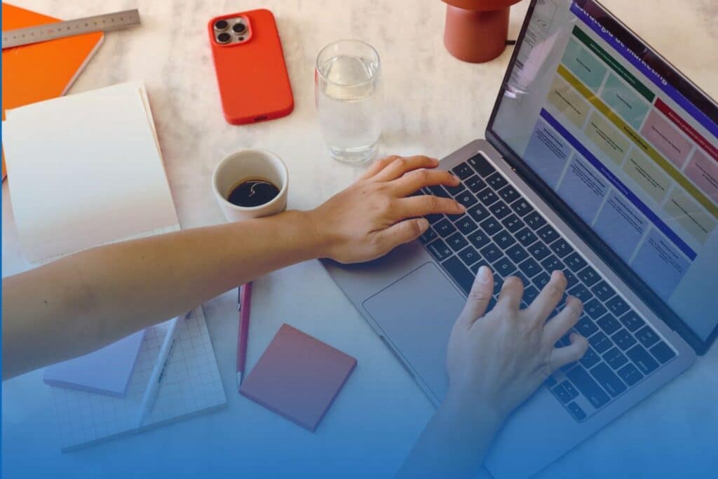 Top-down view of a remote employee typing on a laptop at an organized workspace with a cup of coffee, notebook, and smartphone.