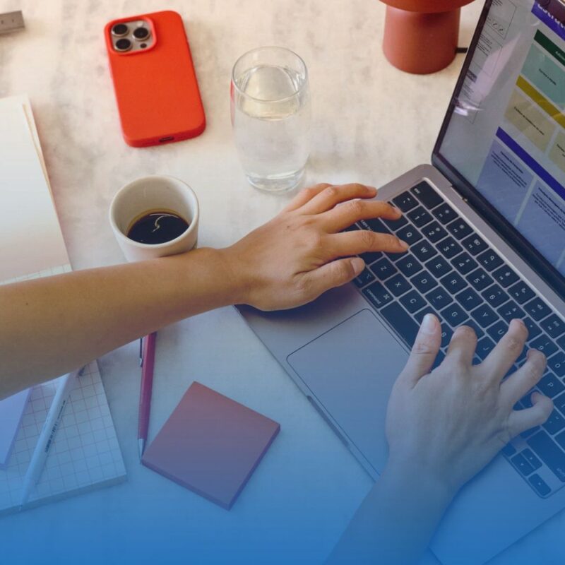Top-down view of a remote employee typing on a laptop at an organized workspace with a cup of coffee, notebook, and smartphone.